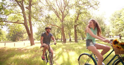 Happy young hipster couple cycling in summer together in a park in Slow Motion, Panning