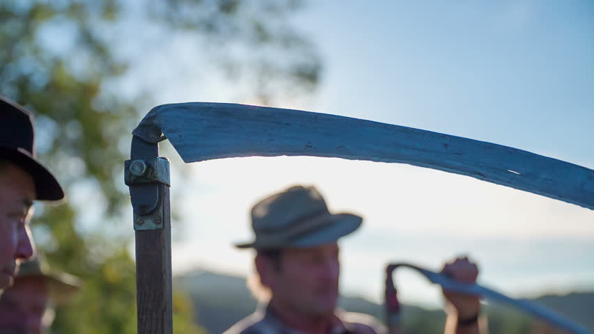 Preparing to start mowing on the sunny day.. Slow motion close up footage of a scythe in the farmers hand standing on the filed and preparing to start mowing on the sunny day.