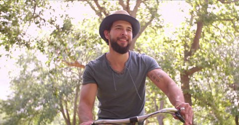 Happy young man laughing and cycling through a sunny park on a summer's day Stock Video