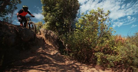 Extreme mountain biker riding over rough terrain steeply dowhill in slow motion