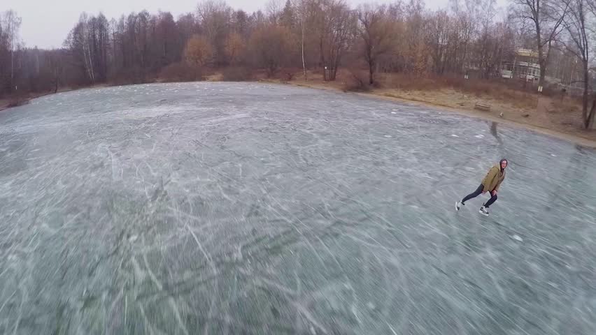 Young man slides on skates on icy pond at winter evening. Aerial view