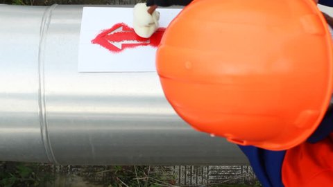 worker draws red arrow on pipes at compressor station of main gas pipeline, timelapse, closeup