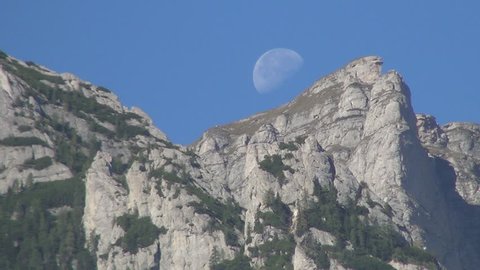 Rocky mountains in sunrise with a monument on top. Big moon in a morning day.