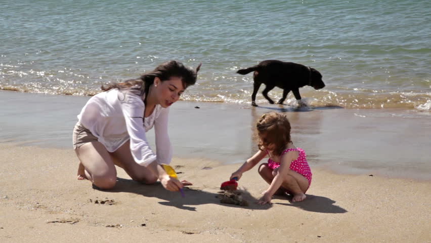 Little Latin girl and her mom relaxing and drawing on the sand together at the beach