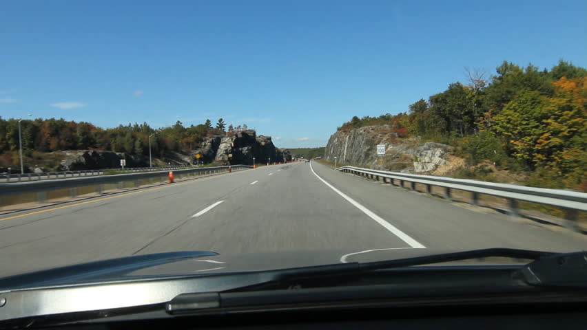 Autumn driving in Northern Ontario. HWY 400 going north driving through rockcut. Canadian flag on the rock at end of clip. Just south of Parry Sound, Ontario.
