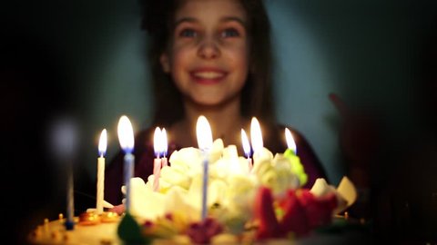 Smiling little girl blows out candles on birthday cake.
