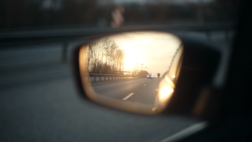 View of the road in the rearview mirror of a car at sunset