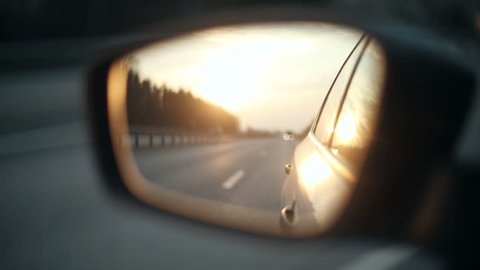 View of the road in the rearview mirror of a car at sunset
