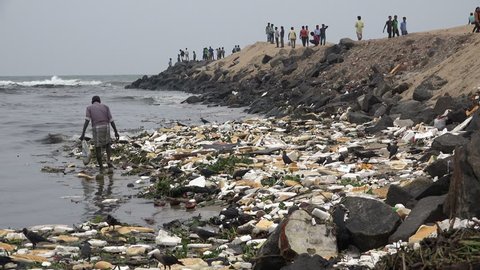 CHENNAI, INDIA - 28 NOVEMBER 2014: An unidentified man searches for items to be recycled on the shores of a beach, as tourists walk to and from a pier, in Chennai.