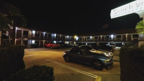 LONG BEACH, CA/USA - March 11, 2015: Generic motel motor lodge at night with people in 4K format. People leave their vehicles in the parking lot and walk to the building for an over night stay.
