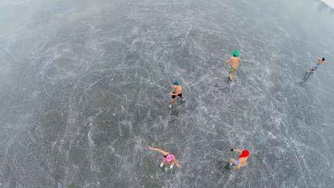 Young men and women in underwear skate on icy pond at winter day. Aerial view in timelapse