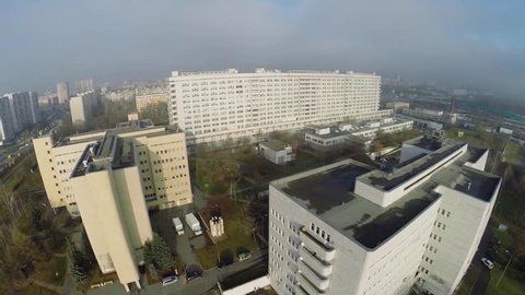 Building complex of clinical hospital and helicopter landing site near street with traffic at autumn cloudy day. Aerial view