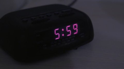 A tired man hits snooze on the alarm clock when it goes off at six o'clock in the morning