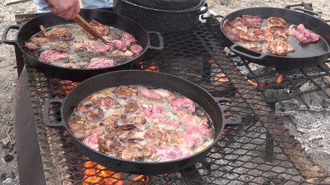 DELTA, UTAH MAR 2015: Cooking lamb chops cast iron pots over camp fire. Meat Mutton and lamb steaks and chops close cooking in cast iron pans over an open outdoor fire. Cowboy and sheep camp bbq.
