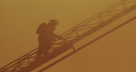 Fireman with self-contained breathing apparatus climbing aerial ladder through thick heavy smoke above fire