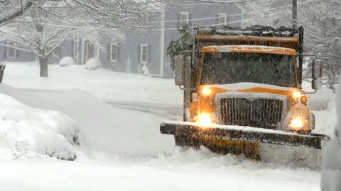 Orange city snow plow coming towards camera on residential street  in a heavy snow storm