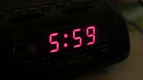 A man hits snooze on an alarm clock when it goes off at six in the morning