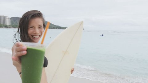 Healthy food and fitness lifestyle woman on beach drinking Green detox vegetable smoothie after surfing workout on summer day on beach. Healthy lifestyle concept with beautiful surfer model. 96 FPS.