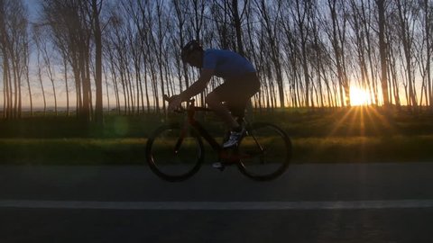 healthy man riding bike working out. training fitness outdoors backlit at the sunset. tracking shot from camera car slowmotion 库存视频