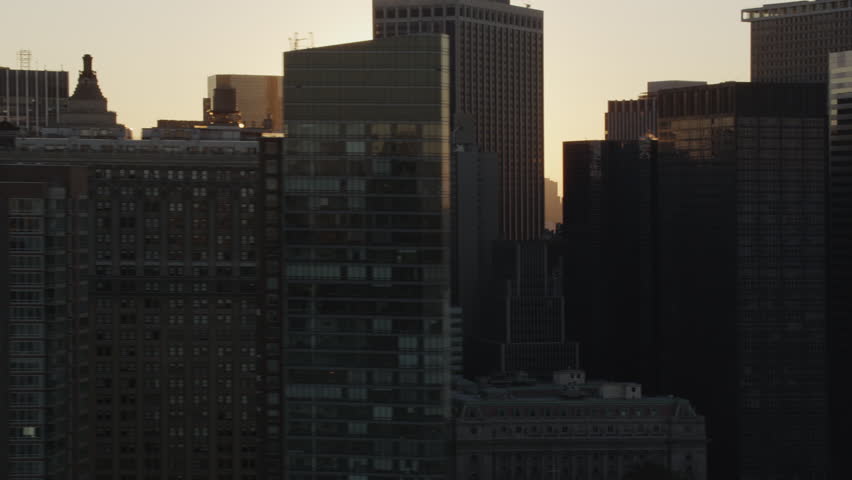 Aerial sunrise New York City skyline view of lower Manhattan and Financial District.  Shot from helicopter with Battery Park and Hudson River in shot.  Bright sun rising through the buildings.  