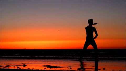 Silhouette of man doing Tai Chi at sunset on the beach.
