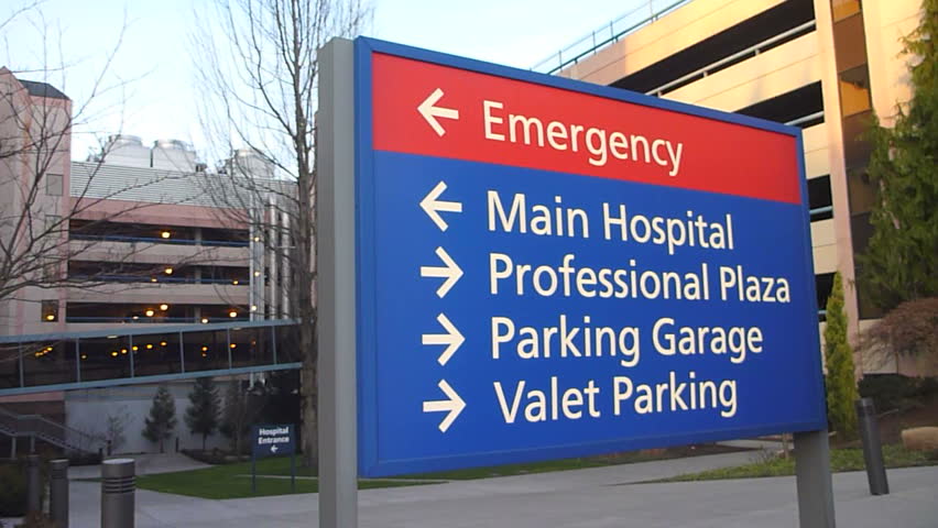 Hospital entrance exterior with sign pointing to emergency, main hospital and parking.