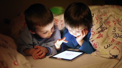 Cute little brothers, playing on tablet in bed at night วิดีโอสต็อก