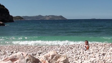 Mother comes and sits with her son on pebbles at the seaside
