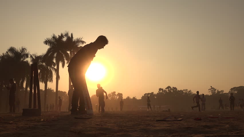 Silhouettes of young men playing cricket in a park in Dhaka, Bangladesh.