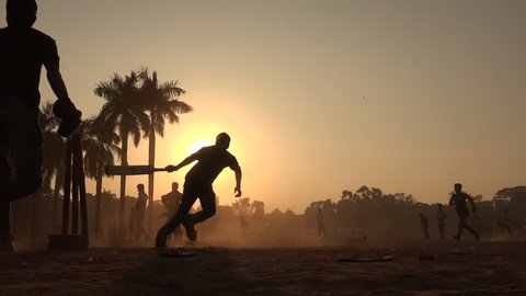 Silhouettes of young men playing cricket in a park in Dhaka, Bangladesh.
