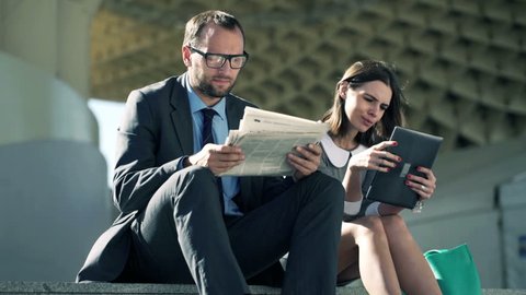 Businesspeople with newspaper and tablet computer sitting on stairs in the city
