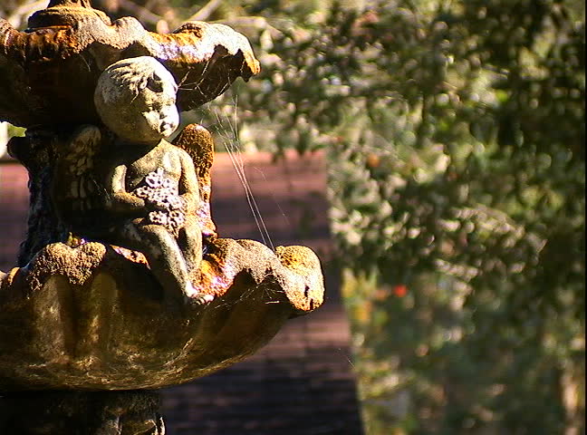 Old fountain and angel statue trickling water in sunlight.