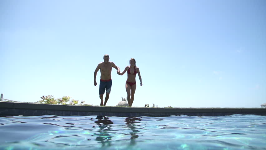 Couple Holding Hands While Jumping Into Swimming Pool 
