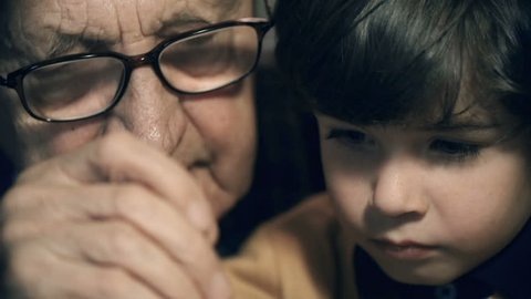 Tilt down the faces of a boy and his grandfather to watch screwdriver and wristwatch details