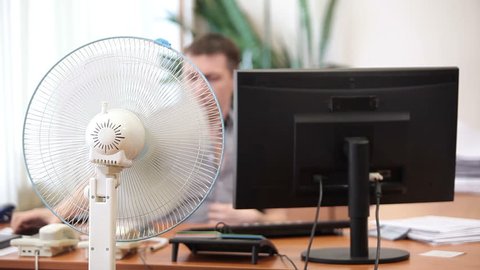 Office heat with cooling fan and perspiring white collar worker leaving his working place