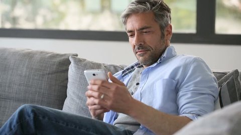 Mature man in sofa reading message on smartphone
