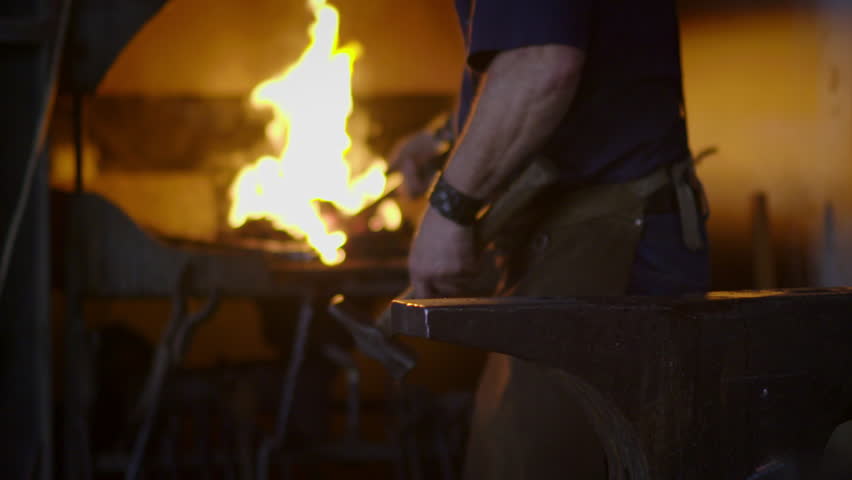 Blacksmith brings dripping hot metal from furnace and creates a shower of sparks as he beats a piece of white hot metal with a hammer on an anvil.  Close up recorded at 180fps. Royalty-Free Stock Footage #9611021
