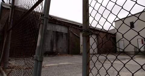 Locked fence at old abandoned industrial building. Camera dollies towards chain and tilts up.