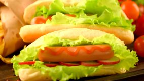 Hot dog with fries on wooden table. Hotdog with fresh buns with grilled sausage, tomatoes, ketchup, mustard, mayonnaise and fresh salad served with French Fries in brown paper. Full HD 1080p. Loopable