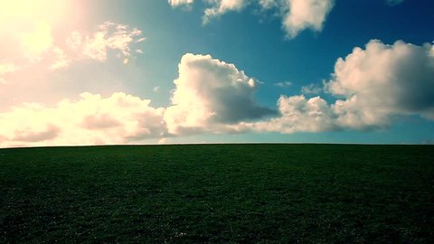 man walking on the edge of a green hill with beautiful clouds above