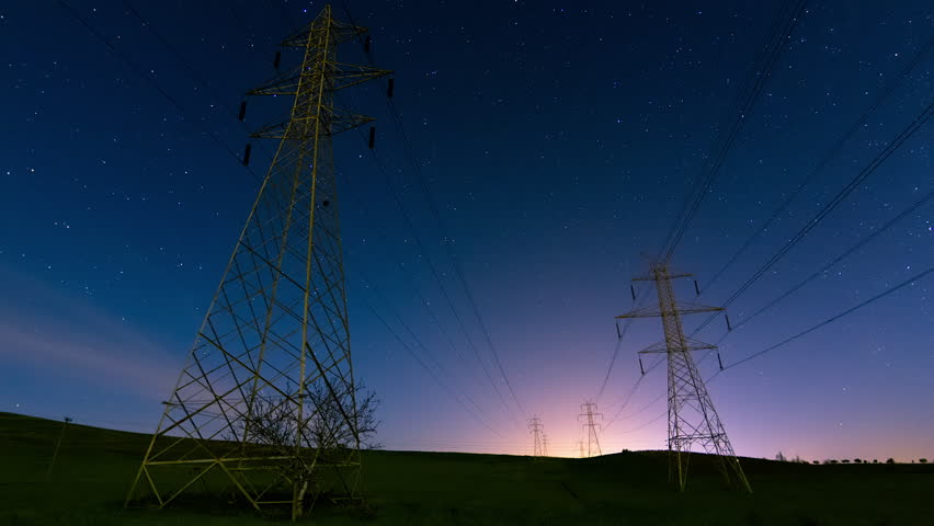 HD timelapse clip of high voltage power lines and tall electricity pylons extending to the horizon against the sky and clouds,in a vast green field in the countryside at night with starry sky. | Shutterstock HD Video #9666491