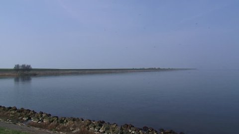 LELYSTAD, THE NETHERLANDS - APRIL 2015: Traffic halfway across Houtribdijk at Trintelhaven + disappears behind the dike at horizon. The dam is part of the Zuiderzee Works.