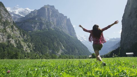 Happy woman having fun running in field nature excited of joy happiness. Joyful active lifestyle with free girl enjoying freedom, Lauterbrunnen valley, Swiss Alps, Switzerland. RED EPIC SLOW MOTION
