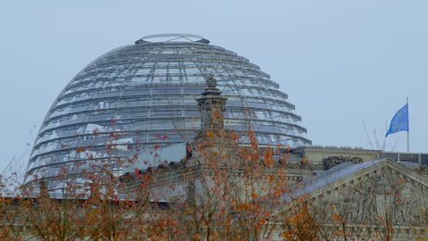Dome with tourist of the Bundestag autumn trees in the foreground Yellow autumn foliage , a European flag waving in the wind

