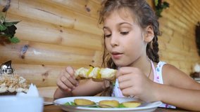 Little girl eats fried meat and smiles in cafe with wooden walls