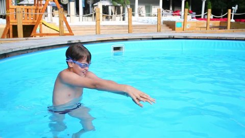 Little boy in swimming goggles swims at aquapark pool.