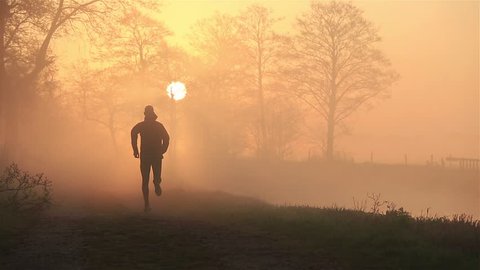 Silhouette of a man running in the countryside during a foggy, spring sunrise.
