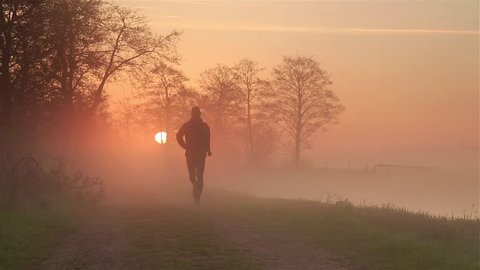 Man (silhouette) running on a gravel road during a foggy, spring sunrise in the beautiful countryside.