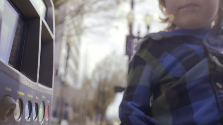 Mom Holds Son And He Presses Buttons At A Pay Station To Help Buy Tickets For Public Transportation