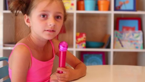 Pretty girl singing into toy microphone sitting at table in game room